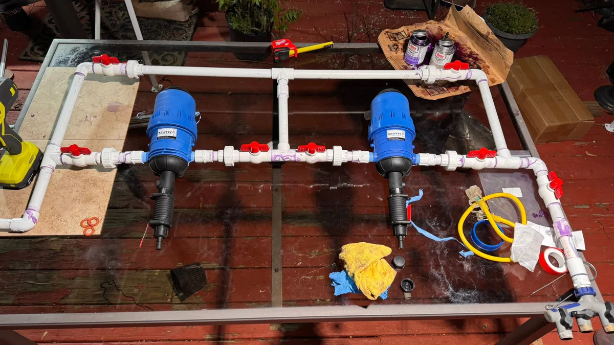The PVC injector manifold laid out on a table during assembly, with PVC primer and cement, tape and tools around it